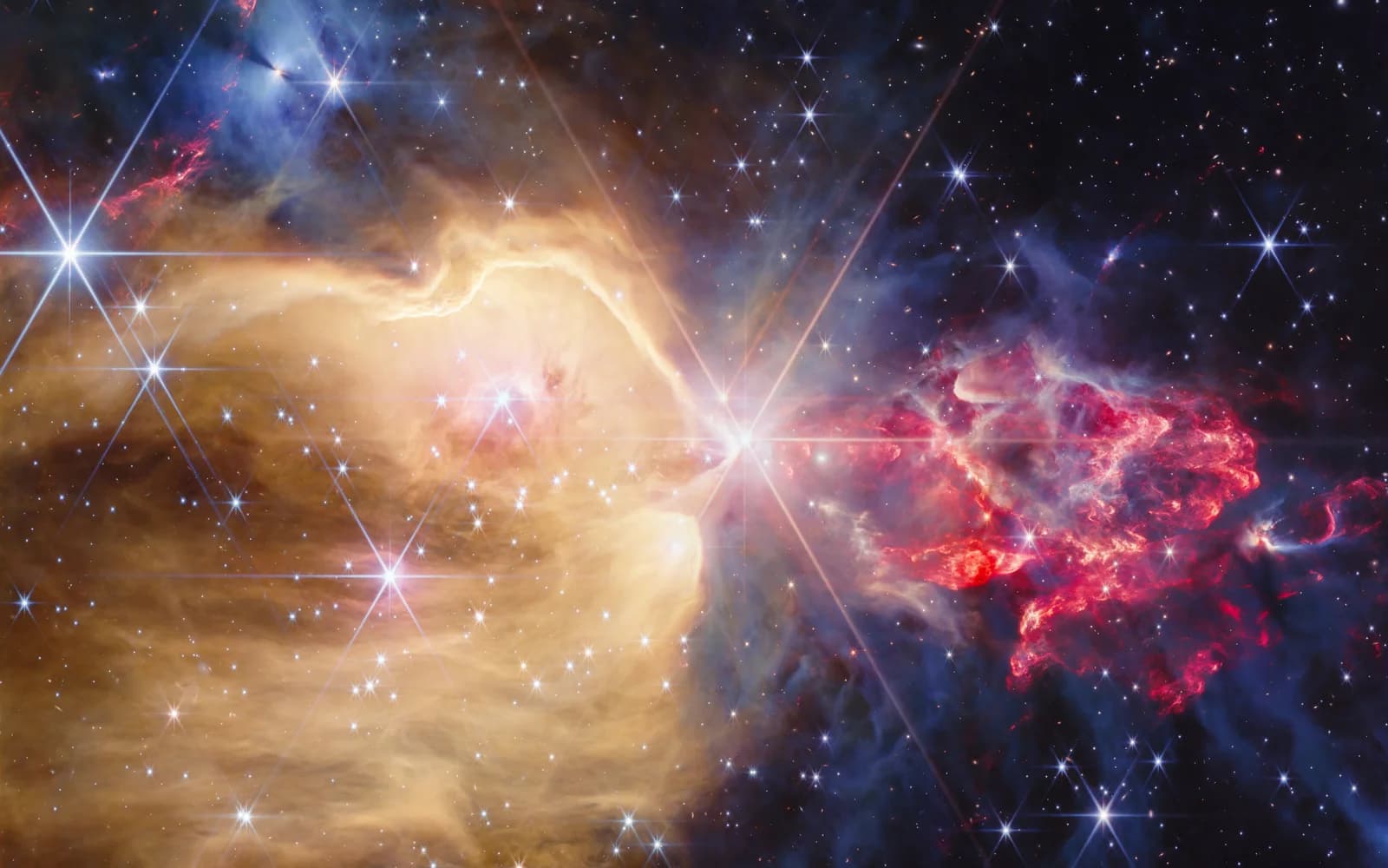 Observación telescópica de NGC 7129 con gas dorado a la izquierda y flujos rojos a la derecha entre estrellas; colores asignados a filtros infrarrojos.