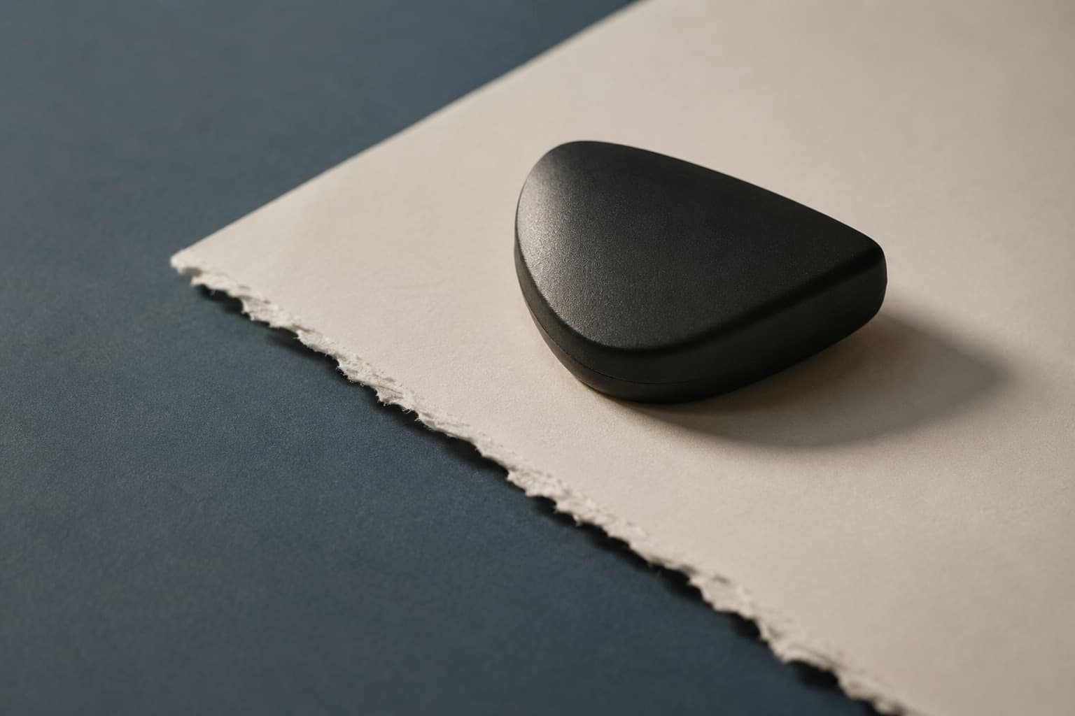 A dark rounded object resting on heavy paper with a torn deckle edge