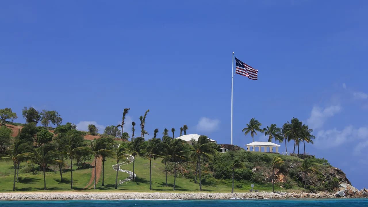 La isla Little Saint James, en las Islas Vírgenes de EE. UU., vista desde el mar: palmeras, edificios blancos y una bandera en un mástil