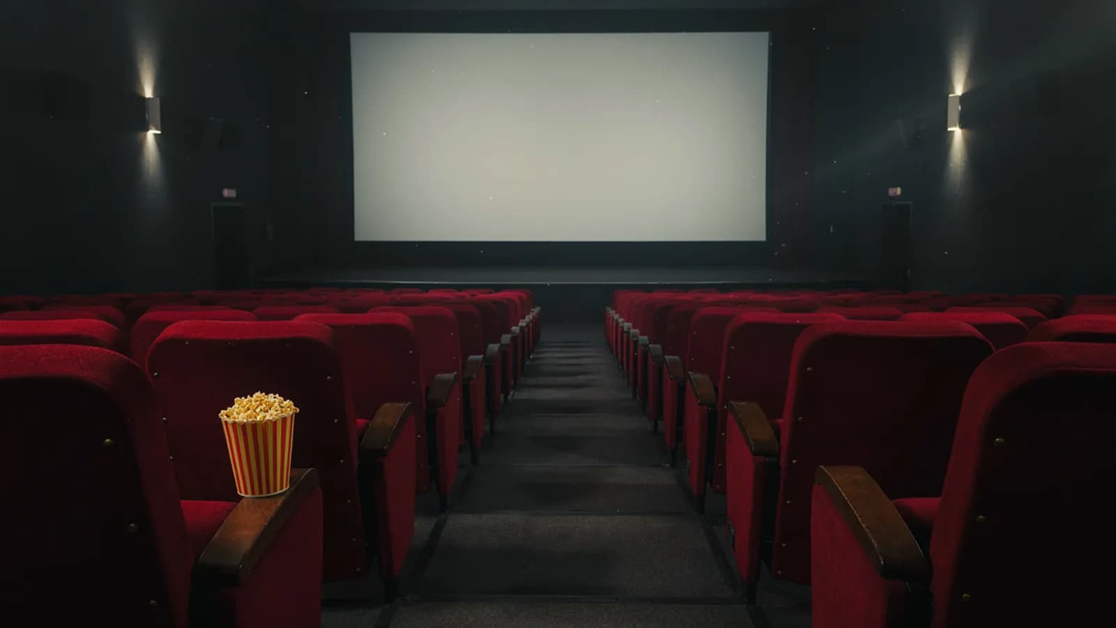 An empty cinema hall with red velvet seats facing a bright blank screen and a bucket of popcorn on one seat; AI-generated illustration
