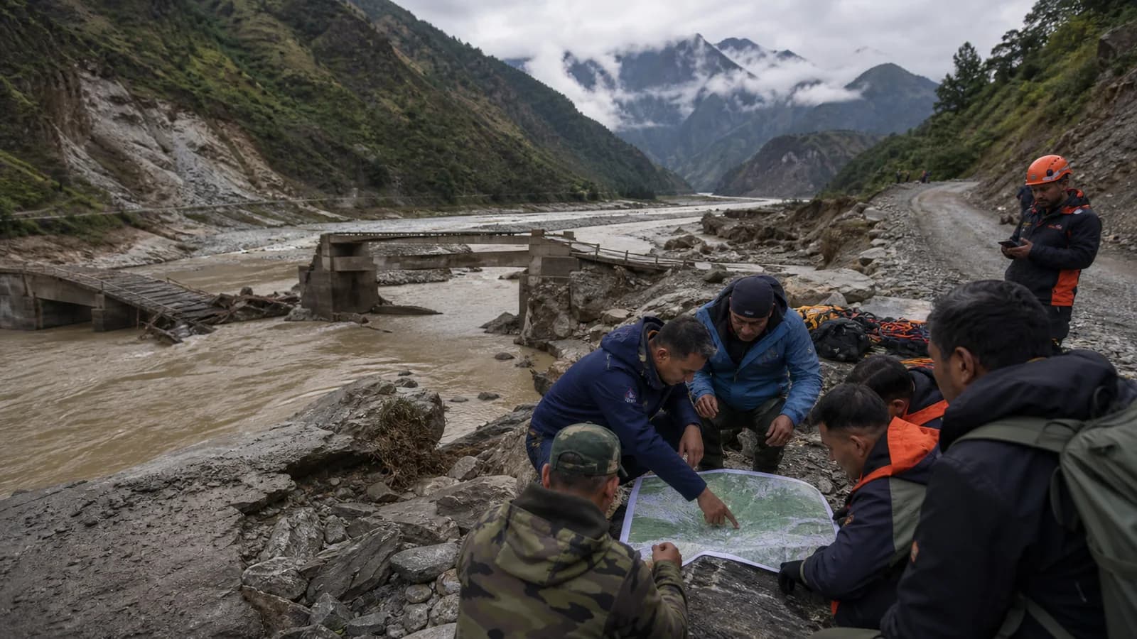 Flood-response teams working beside a damaged mountain road and river valley in Nepal