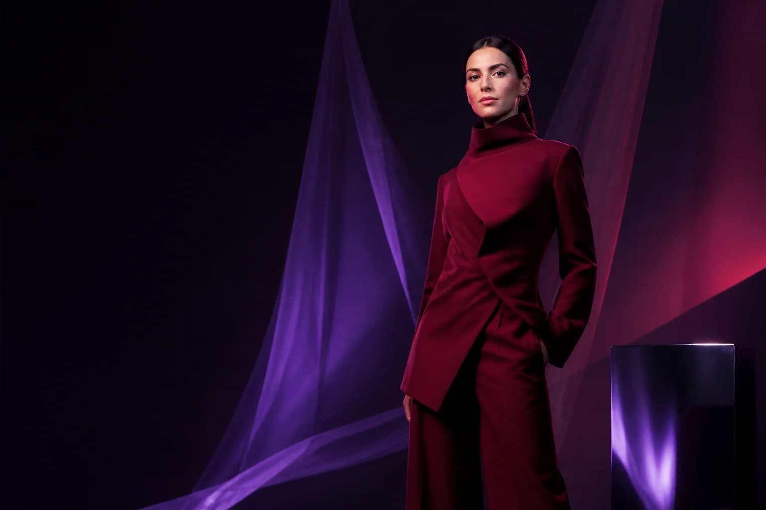 A campaign portrait: a burgundy suit with a sculpted jacket against a dark backdrop streaked with light
