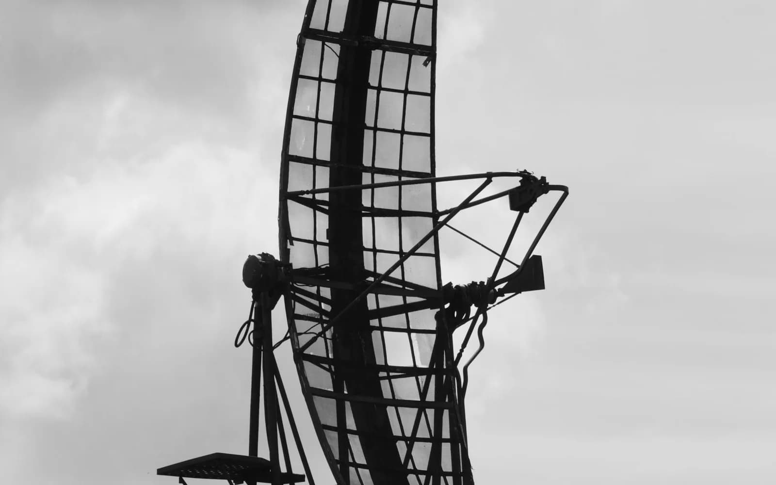 A radar antenna silhouetted against a cloudy sky in monochrome