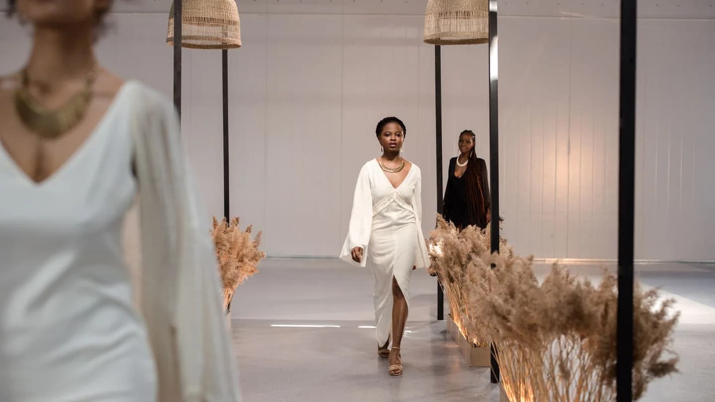 Models walking a minimalist runway lined with dried pampas grass, the nearest in a long white dress with wide sleeves; illustrative photo, not from New York Fashion Week