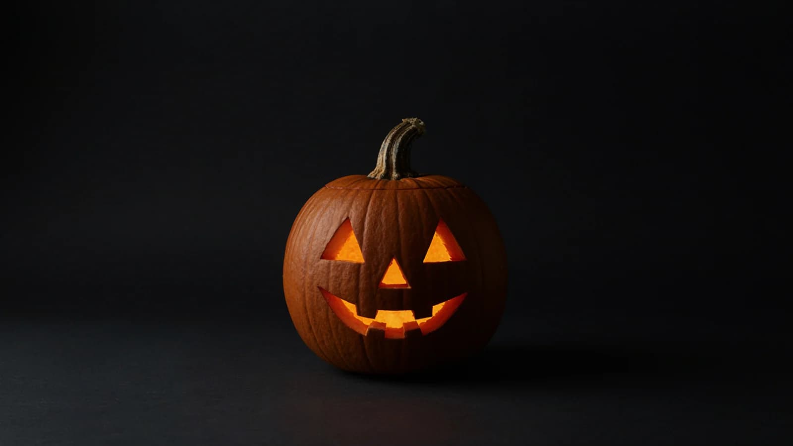 A carved jack-o’-lantern glowing from inside on a plain dark charcoal background; AI-generated image