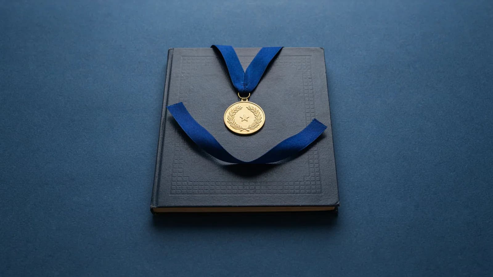 A gold medal on a blue ribbon lying on a closed dark notebook on a plain deep blue background; AI-generated image