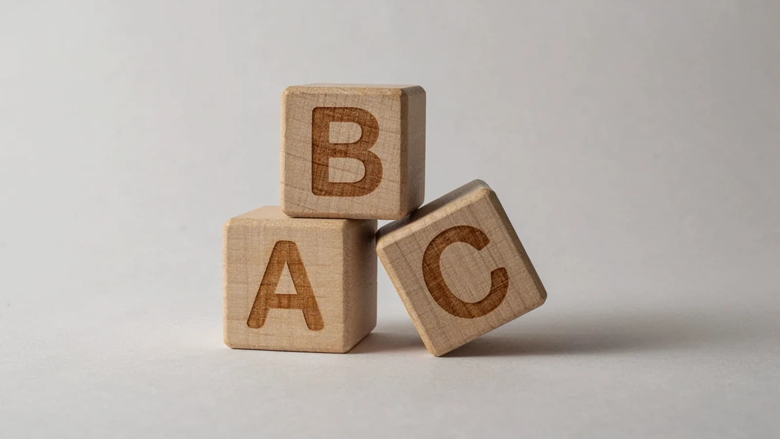 Three wooden toy blocks carved with the letters A, B and C on a plain light-grey background; AI-generated image