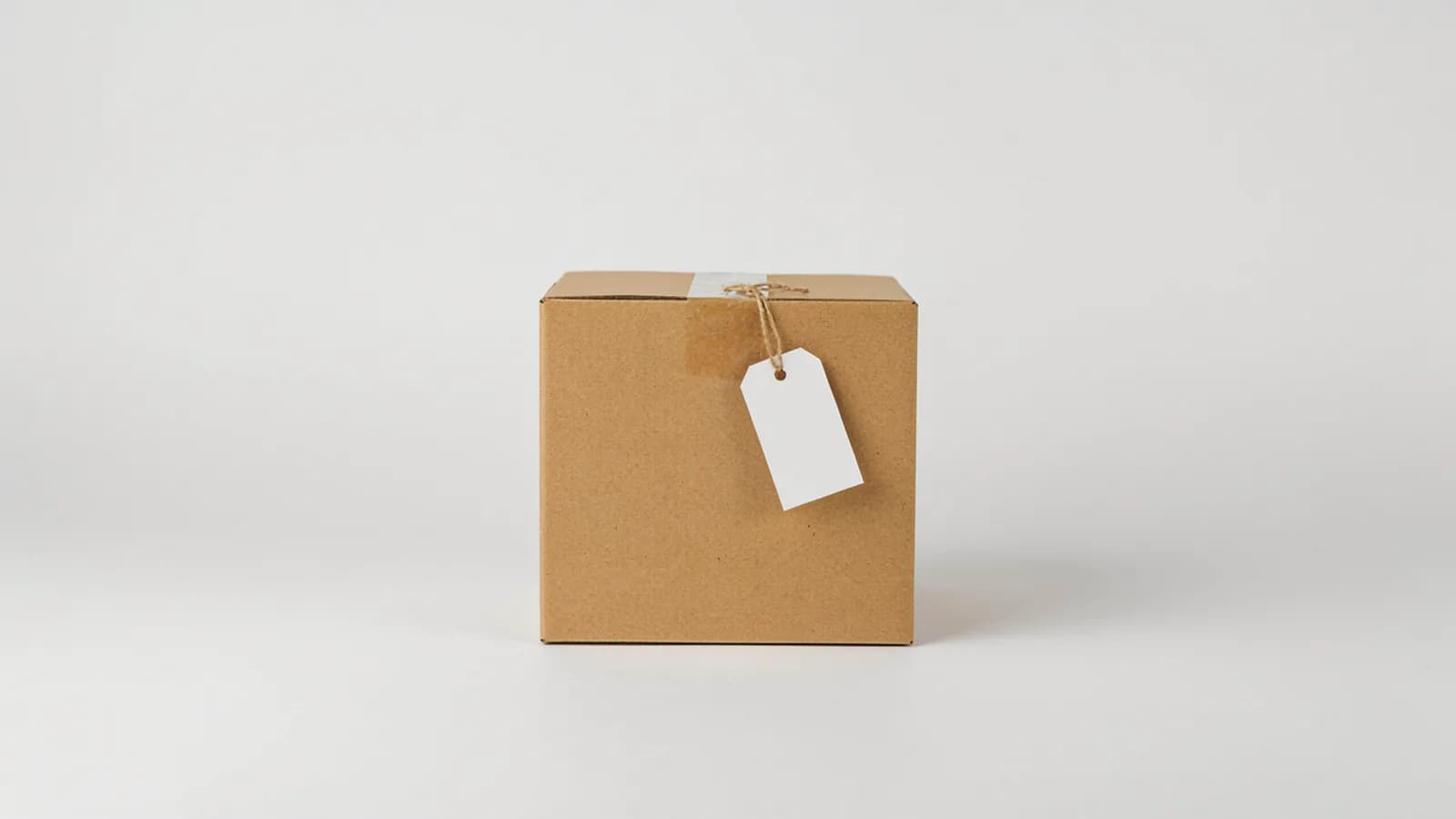 A closed cardboard parcel box with a blank paper tag on a string on a plain white background; AI-generated image
