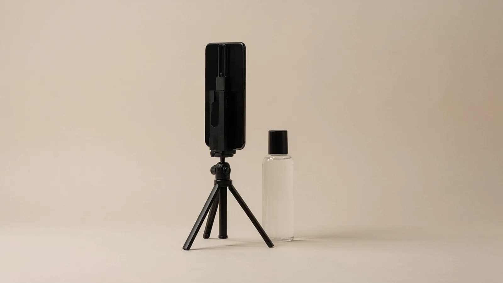 A black smartphone on a small tripod next to a clear cosmetics bottle on a plain beige background; AI-generated image