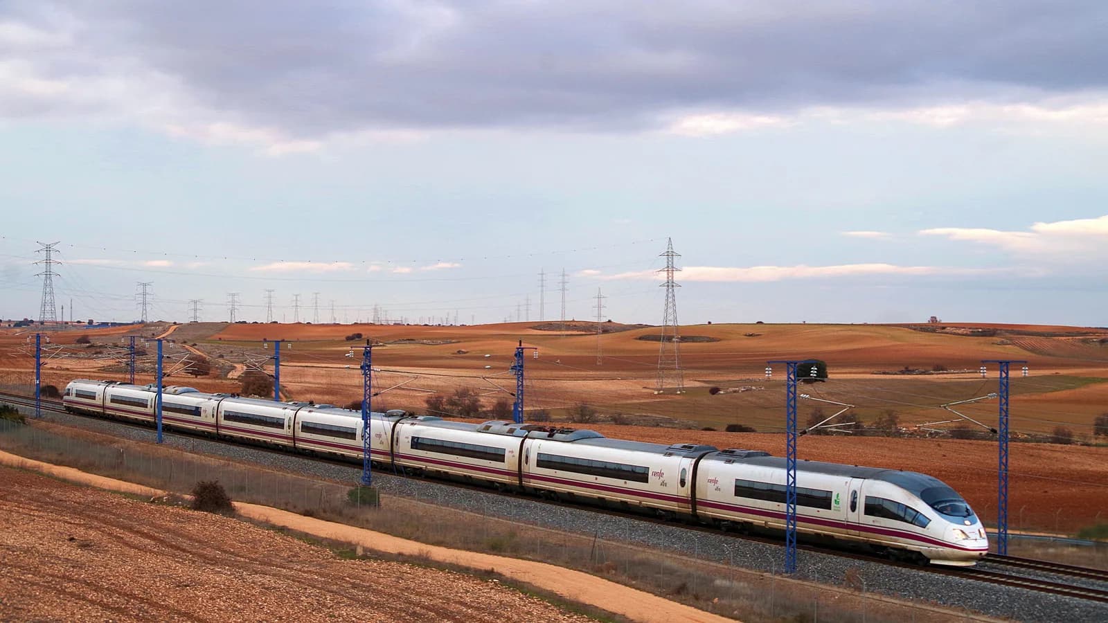 Archive photo: a white Renfe AVE Class 103 high-speed train crossing red farmland near Guadalajara on the Barcelona–Madrid line, not the crash site